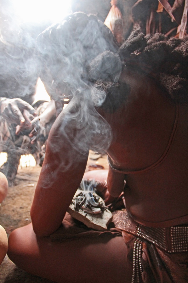 A Himba woman in traditional dress burns myrrh resin as perfume. Kunene, Namibia