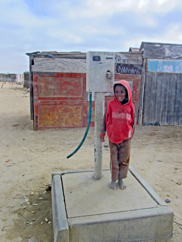 A boy stands by a water pump in Swakopmund, Namibia
